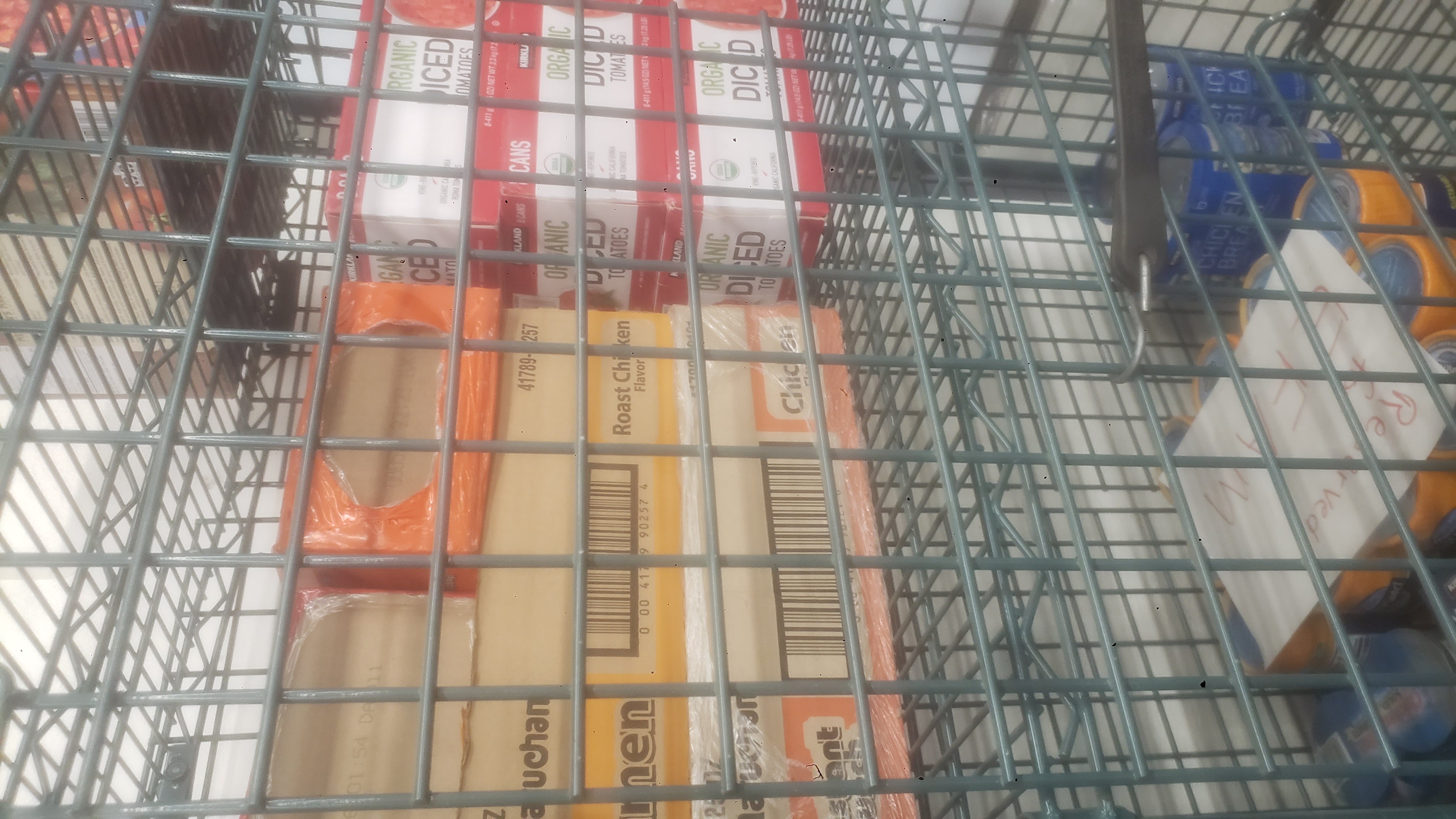 Boxes of ramen noodles, canned meats, and boxes of diced tomatoes in a cage shelf.